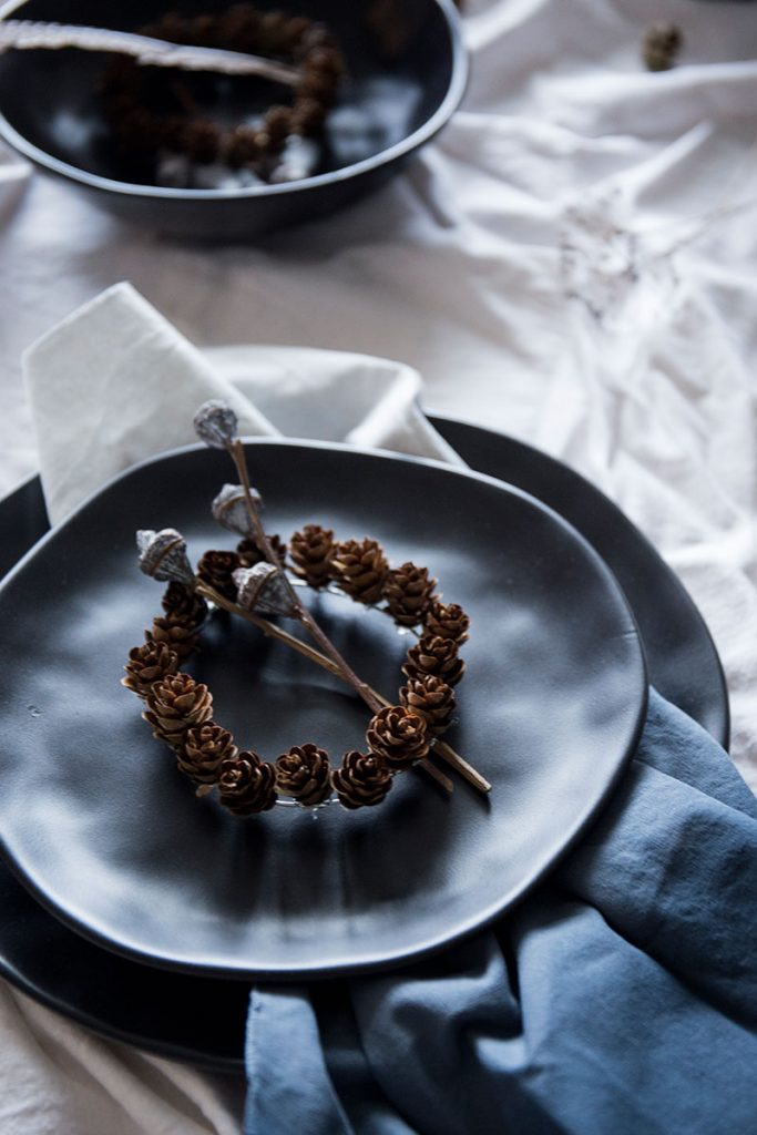 schwarzes-Tongeschirr-mit-DIY-Tannenzapfenkranz