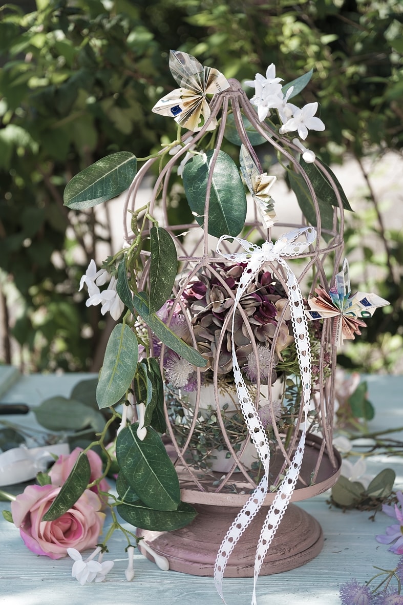 DIY-Geldgeschenk: Dekokäfig geschmückt mit Blumen und gefalteten Geldscheinen