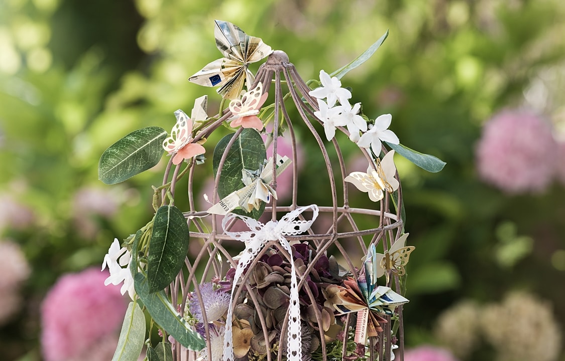 DIY-Geldgeschenk: Dekokäfig geschmückt mit Blumen und gefalteten Geldscheinen