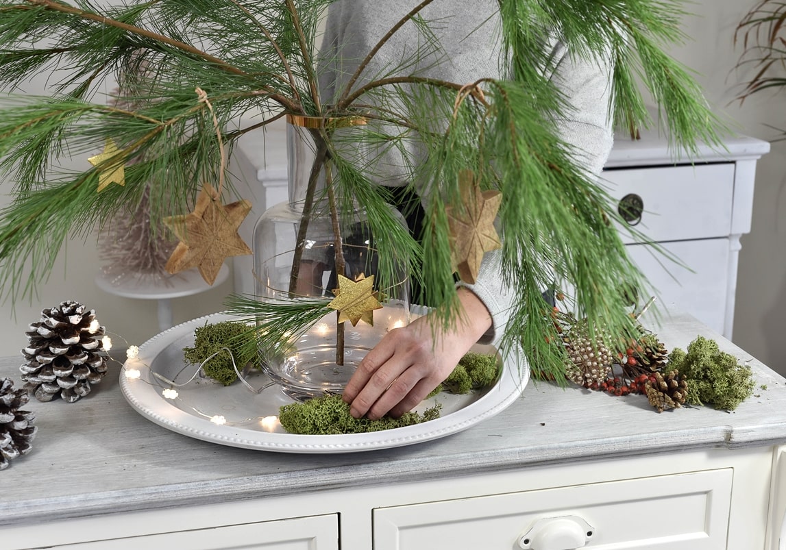 Dekoteller mit Moos und anderen Naturmaterialien auslegen.