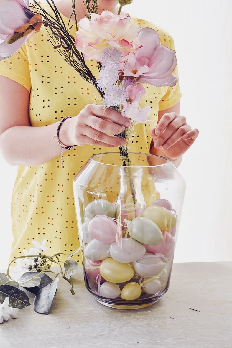 Ostereier und Blumen in die Vase geben